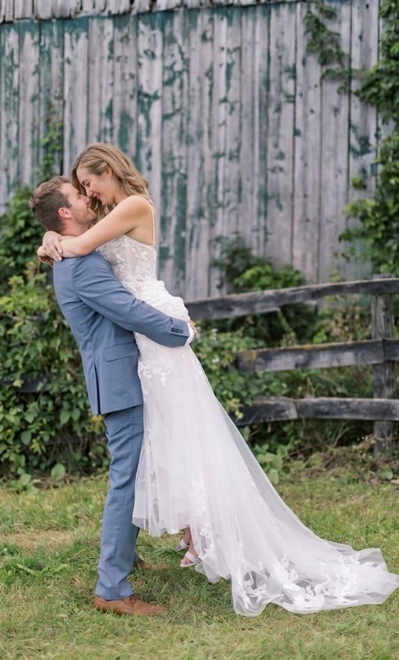 Bride and groom sharing a laughing embrace in front of a rustic barn