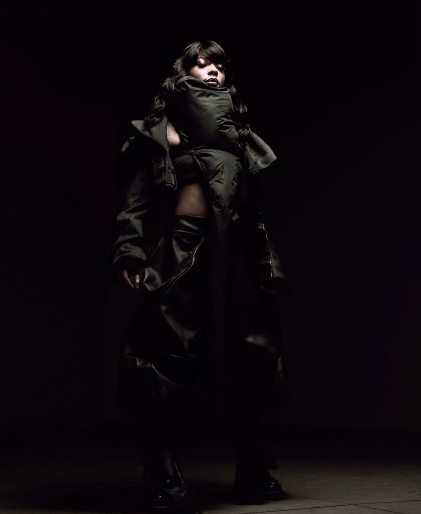 Full-length look in a voluminous quilted coat, lit by a single beam of light