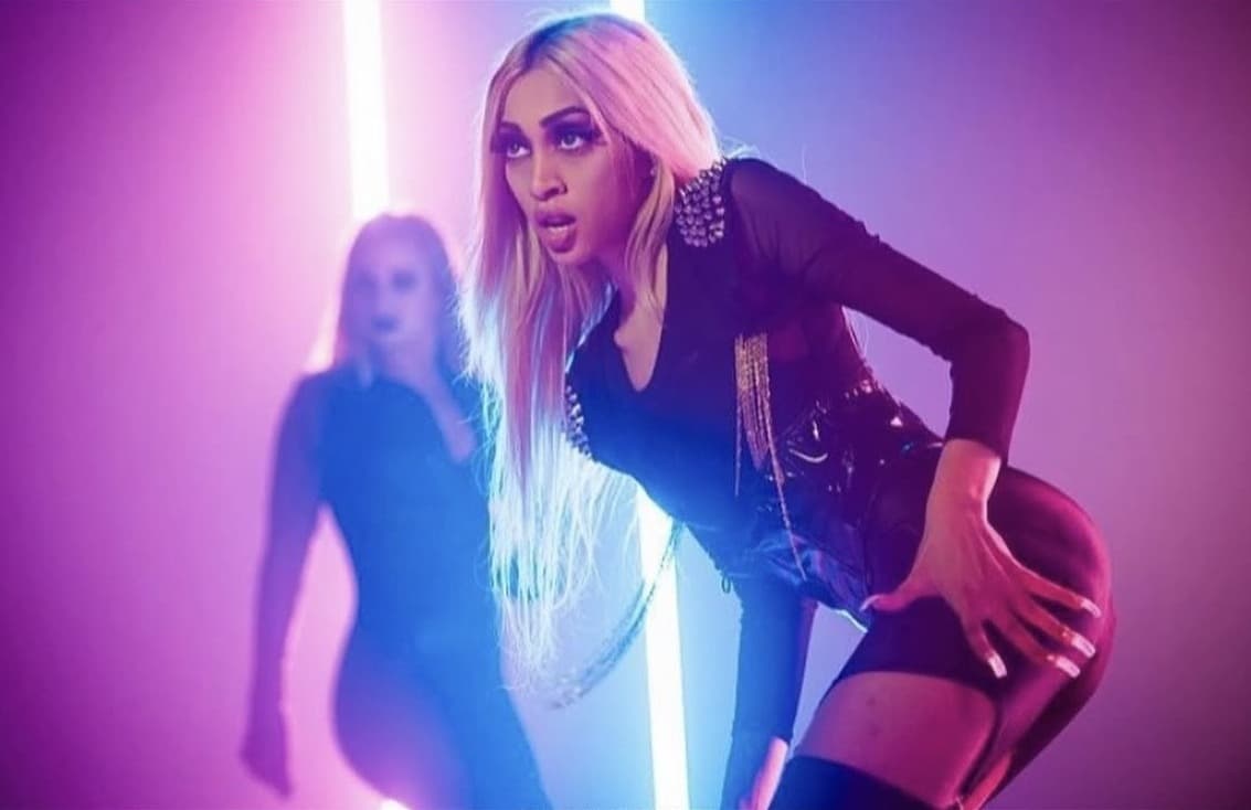 Music-video set still under pink and blue neon with dramatic smoked-out glam