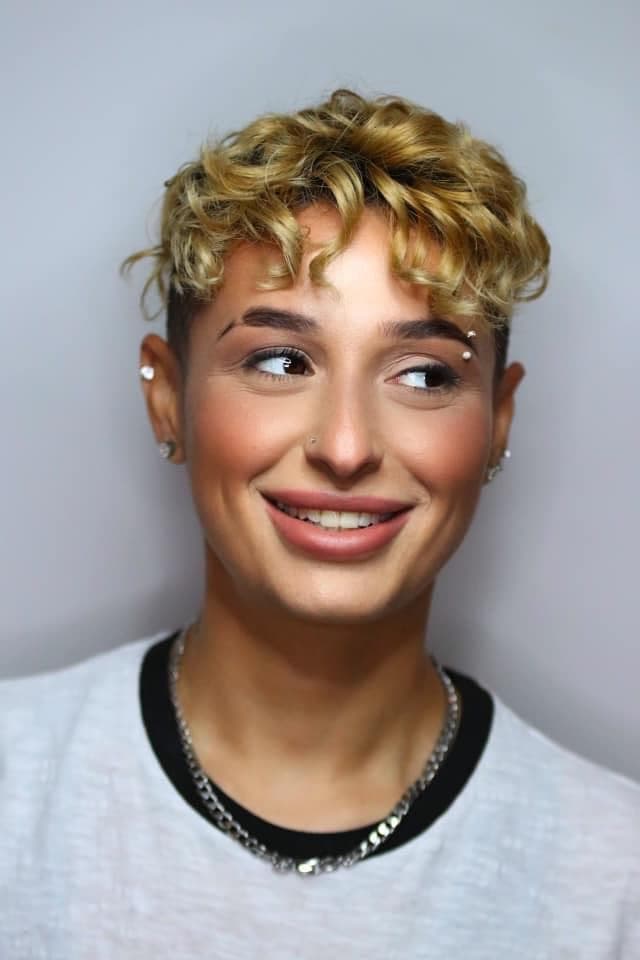 Studio portrait with soft bronzed glam and sculpted brows under curly blonde hair